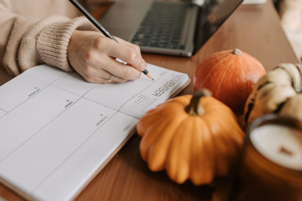 journaling on a desk, next to a computer and a pumpkin